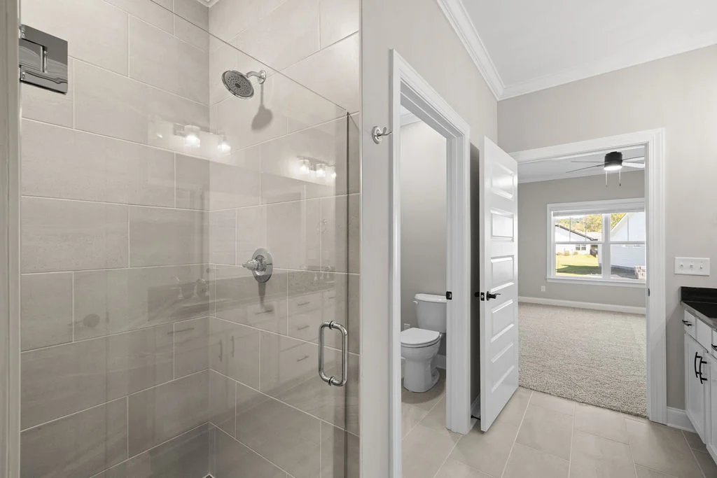 Modern bathroom with glass shower, adjacent to a white bedroom. Design by Pratt Home Builders in Chattanooga TN.