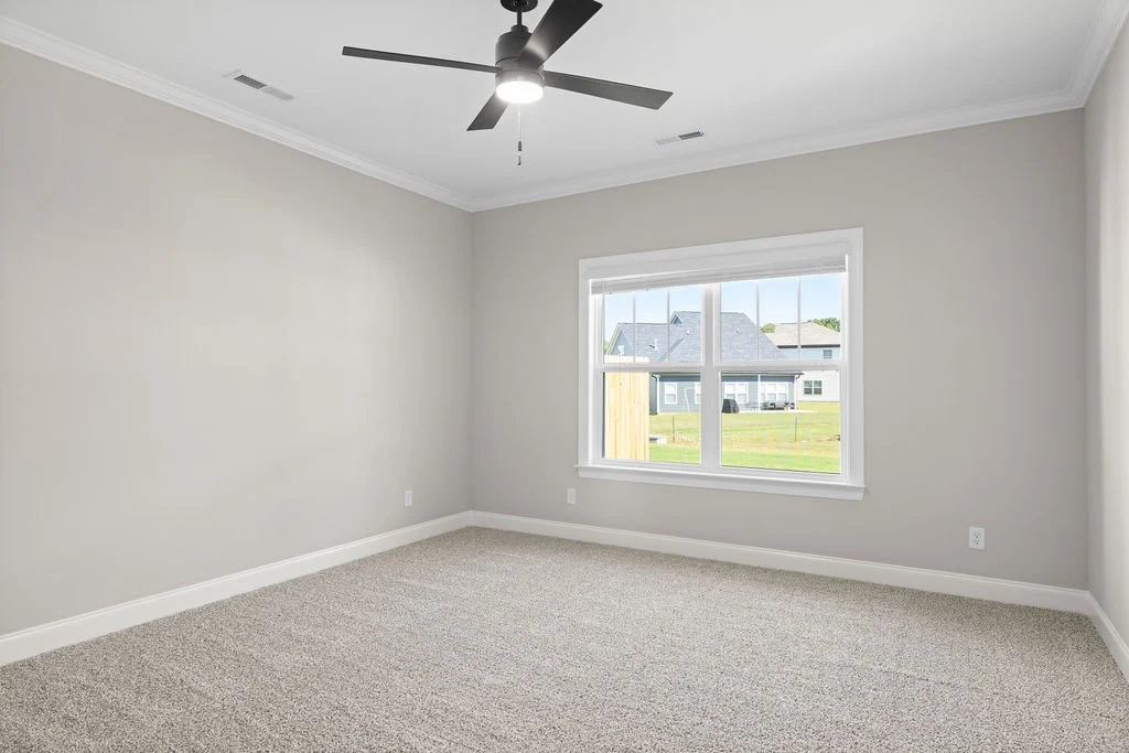 Empty room with beige walls, gray carpeting, large window, ceiling fan, by Pratt Home Builders in Chattanooga TN.