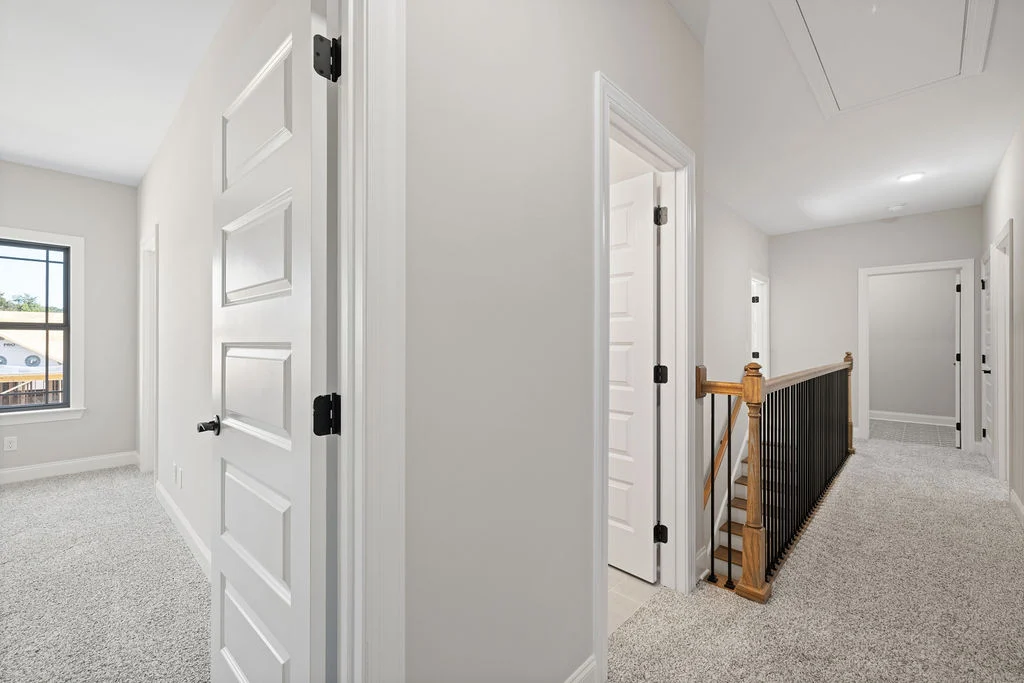 Spacious upstairs hallway in modern home by Pratt Home Builders in Chattanooga, TN, featuring pristine white walls and elegant railing.