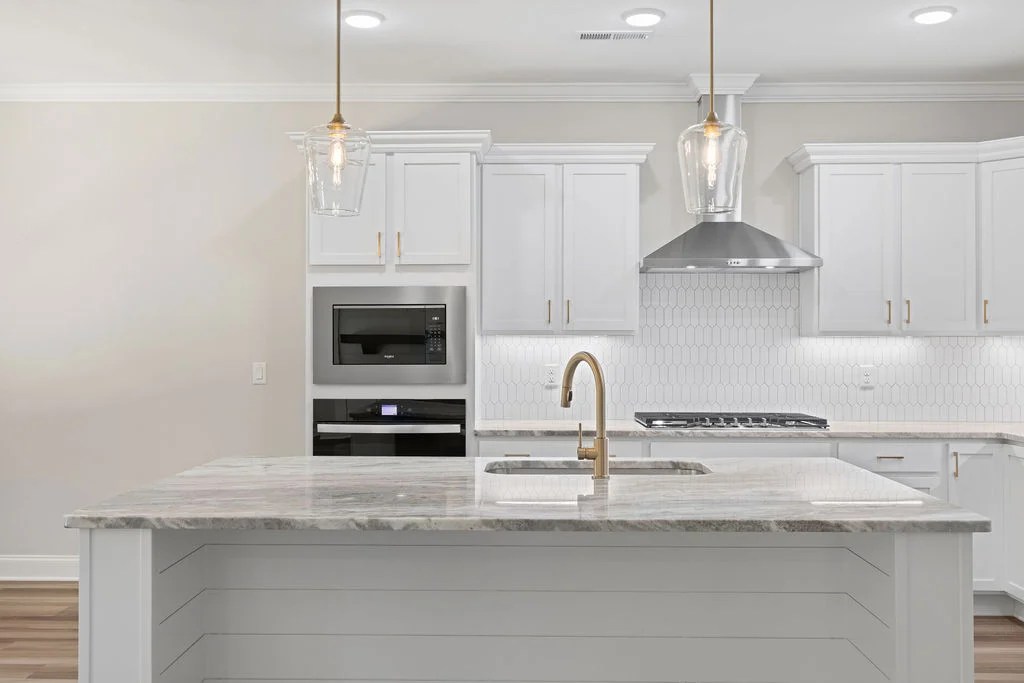 Modern kitchen with white cabinets, marble island, pendant lights, and a gold faucet. Designed by Pratt Home Builders in Chattanooga TN.