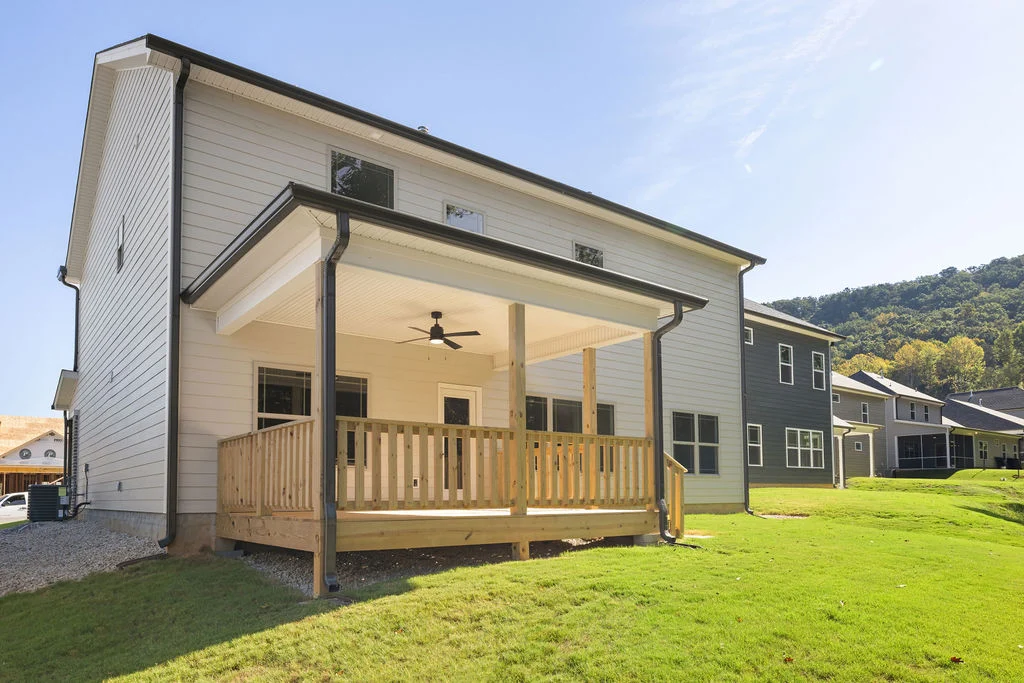Two-story home with covered porch, ceiling fan, and wooden railing. Part of Pratt Home Builders in Chattanooga, TN, nestled near green hills.