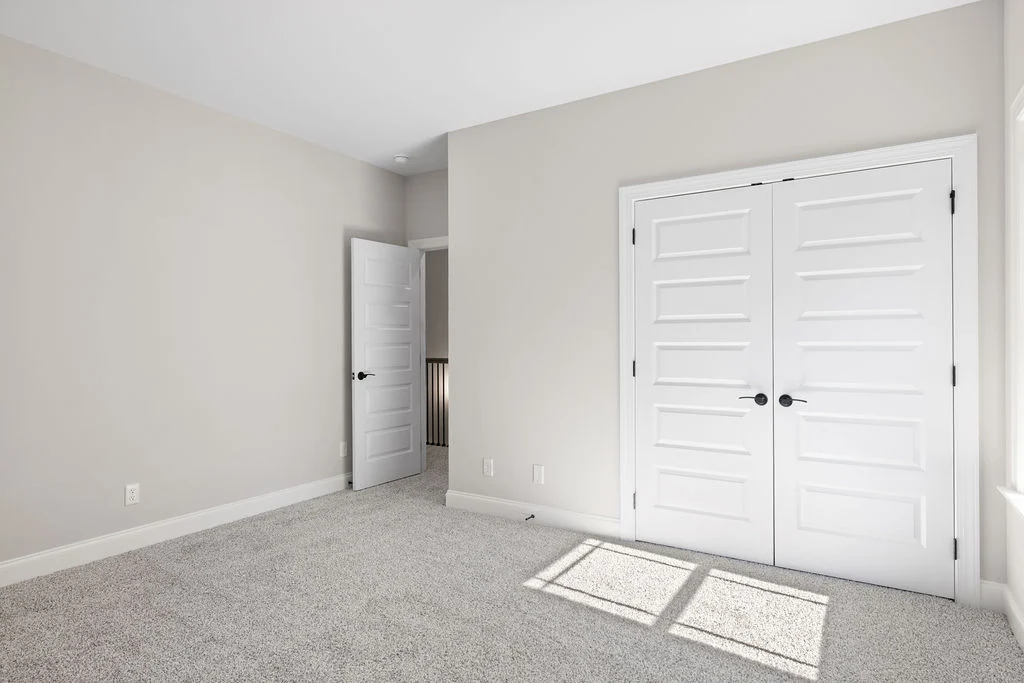Bright, empty room with gray carpet, white walls, double closet doors, and a single open door. Pratt Home Builders in Chattanooga TN.