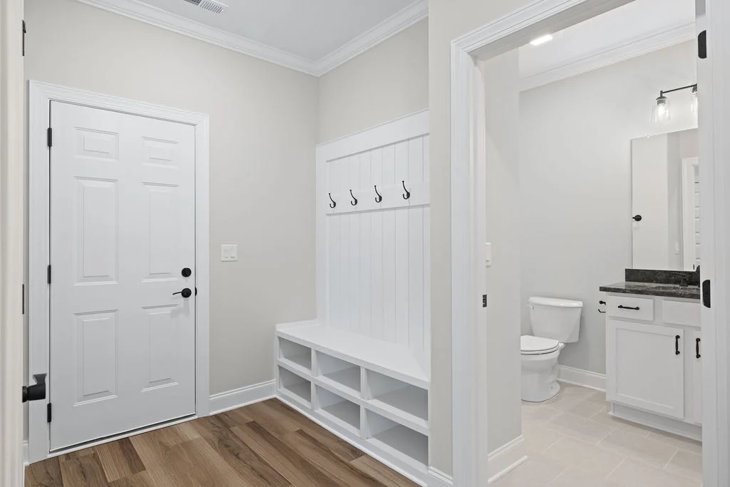 Entryway with white door, bench with hooks, and access to a bathroom. Designed by Pratt Home Builders in Chattanooga TN.