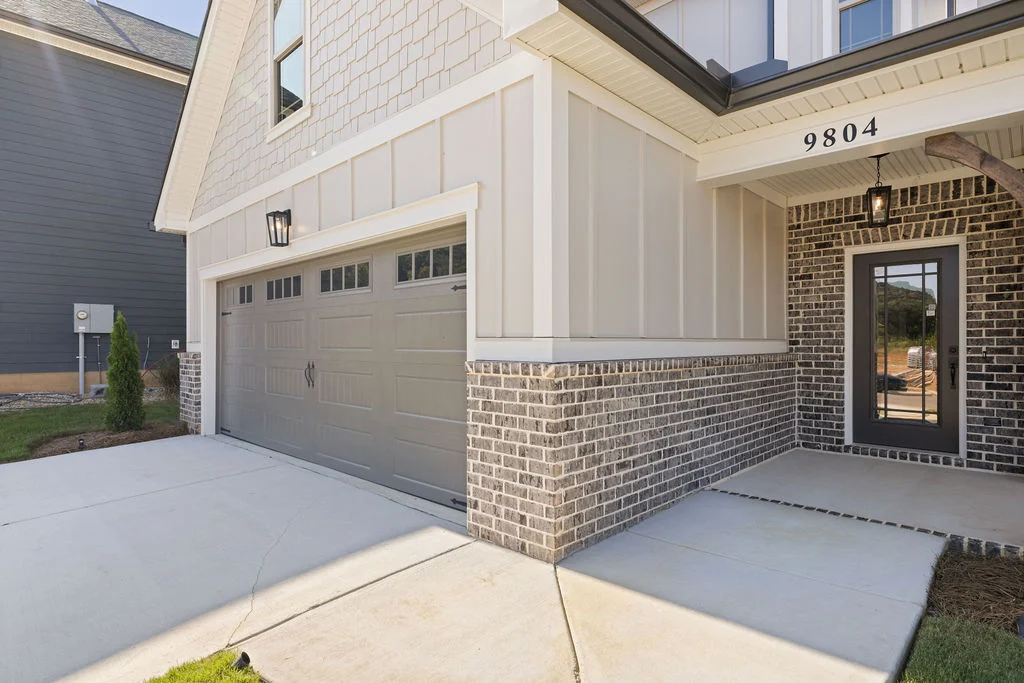 Modern home exterior with brick and panel siding, featuring a garage and front door. Design by Pratt Home Builders in Chattanooga TN.