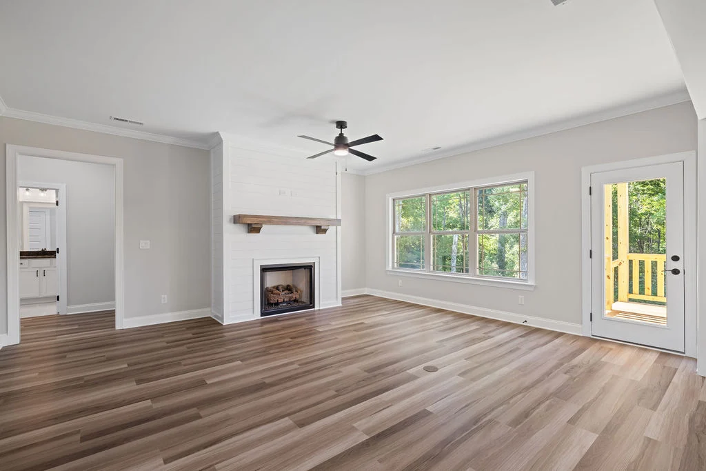 Spacious living room by Pratt Home Builders in Chattanooga TN, featuring wood floors, shiplap fireplace, ceiling fan, and a large window with forest v