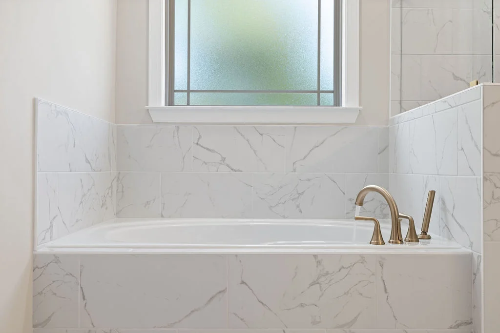 Luxurious bathroom with a marble tub, elegant brass fixtures, and a frosted window by Pratt Home Builders in Chattanooga TN.