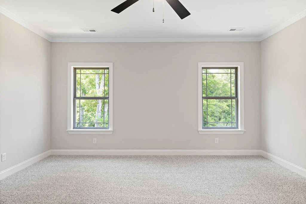 Empty room with gray carpet, two large windows, light gray walls, and ceiling fan. Built by Pratt Home Builders in Chattanooga TN.