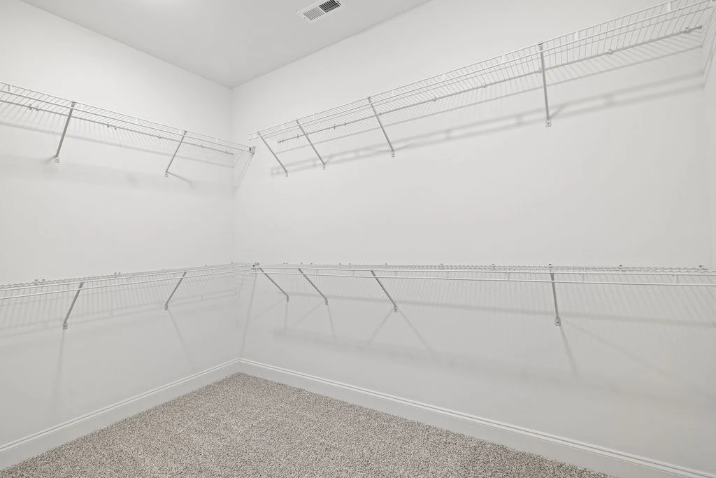 Spacious walk-in closet with white wire shelving, carpet flooring. Designed by Pratt Home Builders in Chattanooga TN.