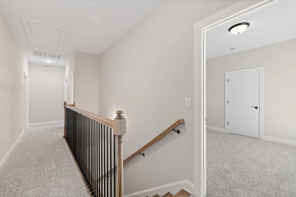 Bright, carpeted upper hallway with wooden railing and door openings, showcasing Pratt Home Builders in Chattanooga TN.