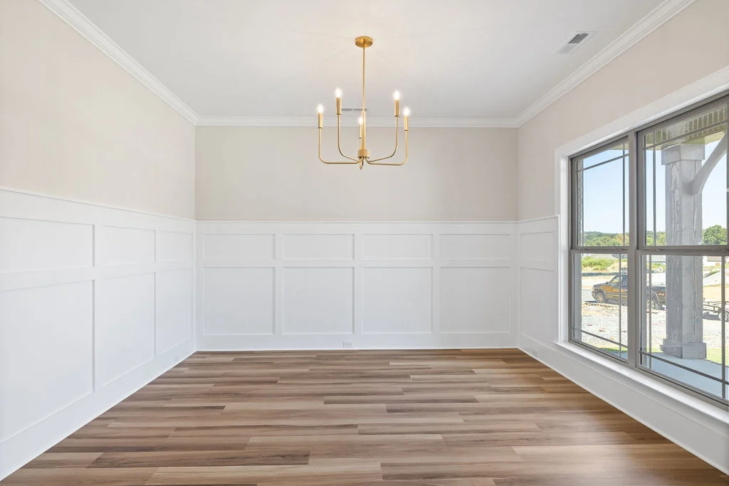 Bright dining room with wainscoting, wood flooring, and large window. Elegant chandelier overhead. Pratt Home Builders in Chattanooga, TN.