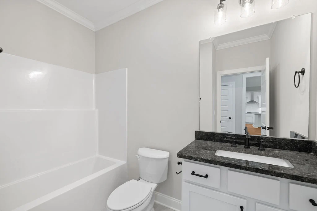 Bathroom with a white tub, a granite countertop, and modern fixtures. Designed by Pratt Home Builders in Chattanooga TN.