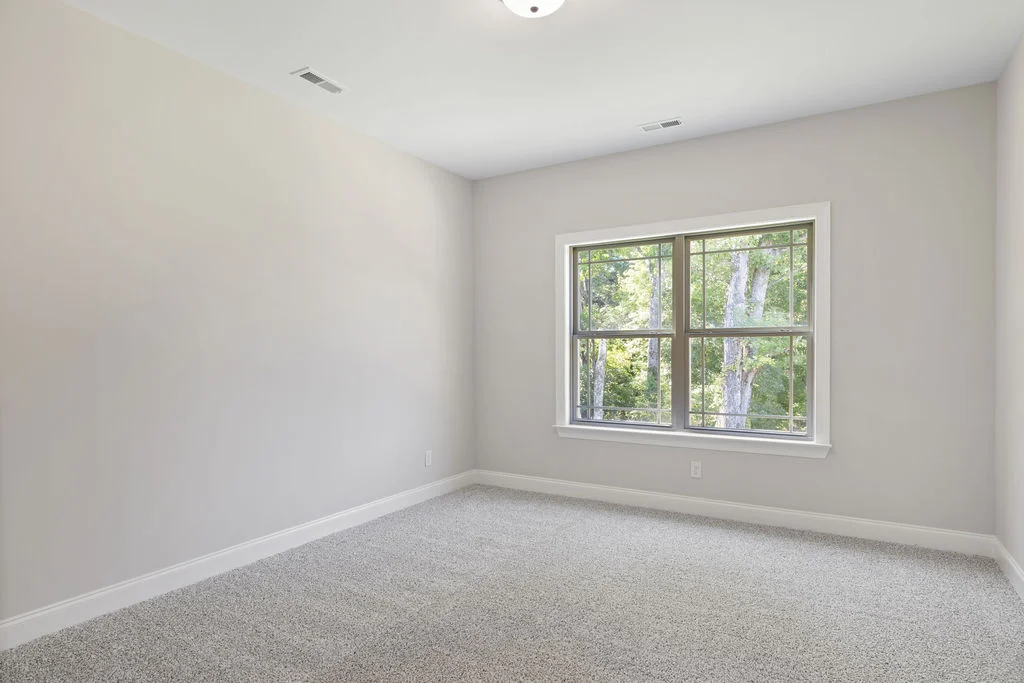 Bright, empty room with gray carpet, large window, and beige walls by Pratt Home Builders in Chattanooga, TN.