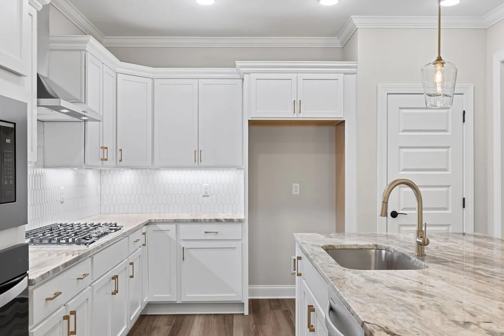 Modern kitchen with white cabinets, marble countertops, and gold accents. Features a hanging light fixture. Pratt Home Builders in Chattanooga TN.
