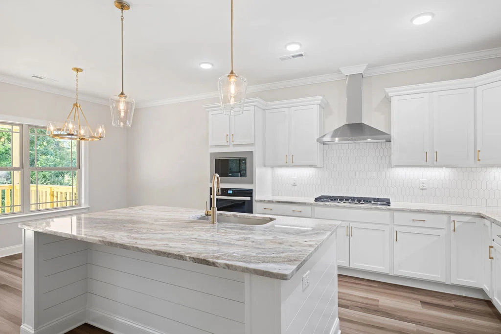 Modern kitchen with white cabinetry, marble island, stainless steel appliances, and pendant lighting by Pratt Home Builders in Chattanooga TN.