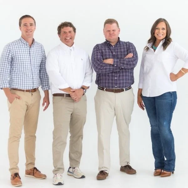 Four people smiling, casually dressed, standing together against a white background, representing Pratt Home Builders in Chattanooga TN.