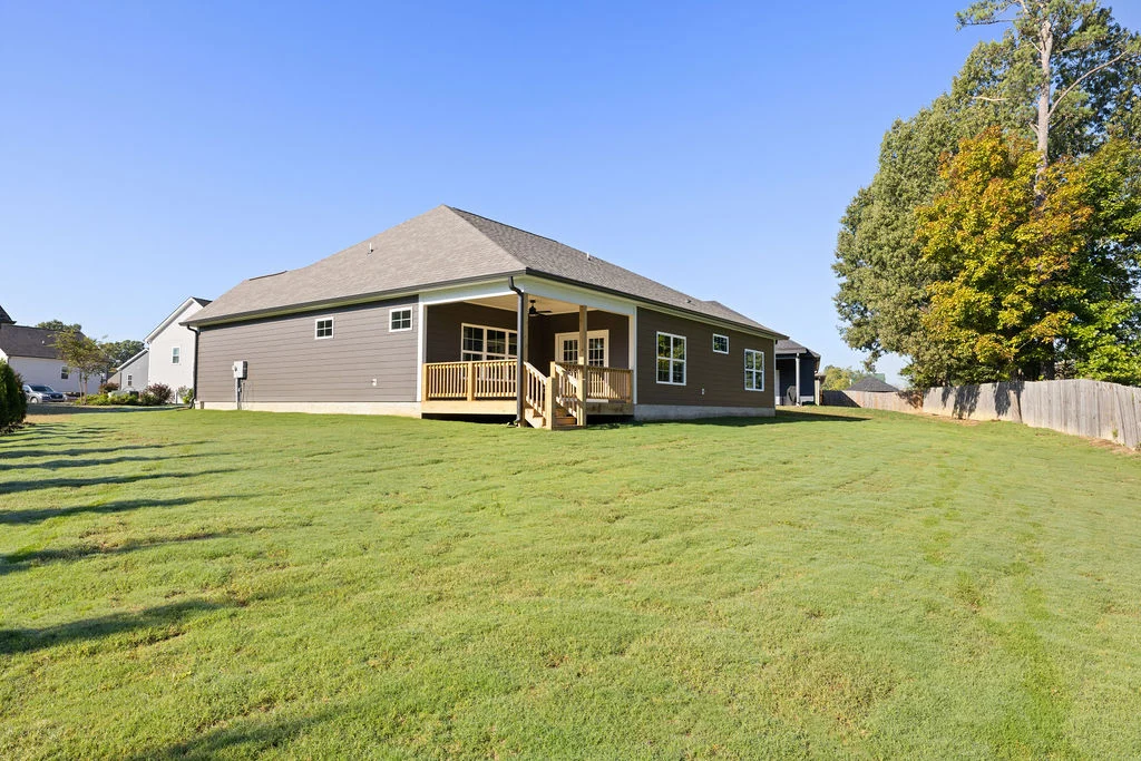 Single-story house with a spacious backyard, constructed by Pratt Home Builders in Chattanooga, TN, featuring a covered back porch and wooden deck.