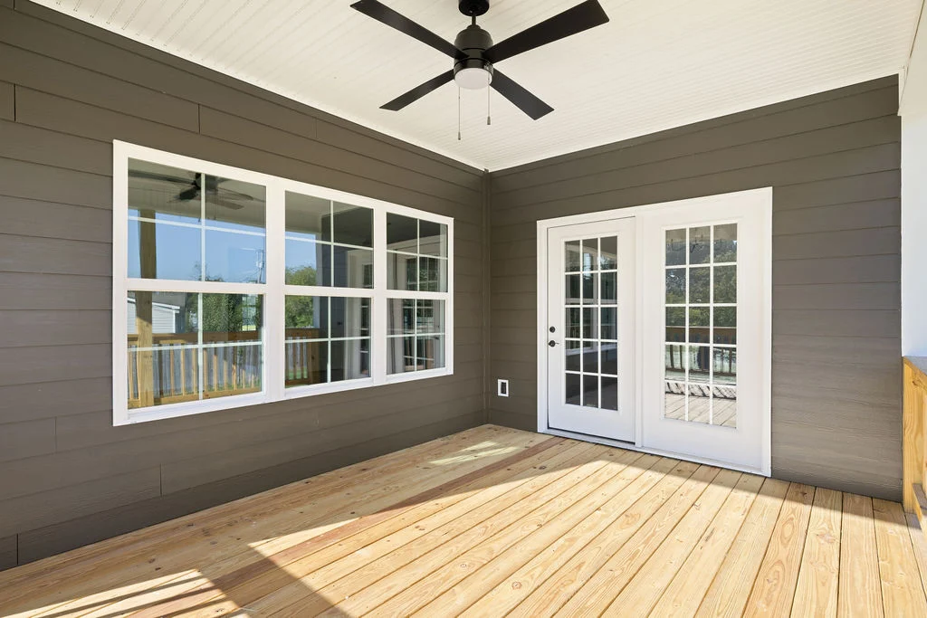 A covered porch with wood decking, white-framed windows, and doors by Pratt Home Builders in Chattanooga, TN, featuring a black ceiling fan.