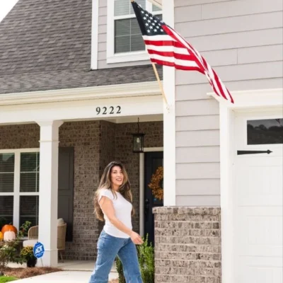 Woman walking past a home with a U.S. flag, number 9222 visible. Front porch has autumn decor. Built by Pratt Home Builders in Chattanooga TN.