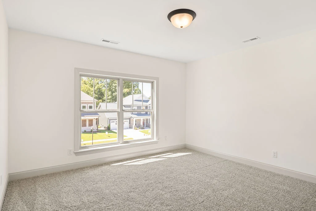 Empty, carpeted room with large window overlooking suburban street; natural light fills the space. Pratt Home Builders in Chattanooga TN.