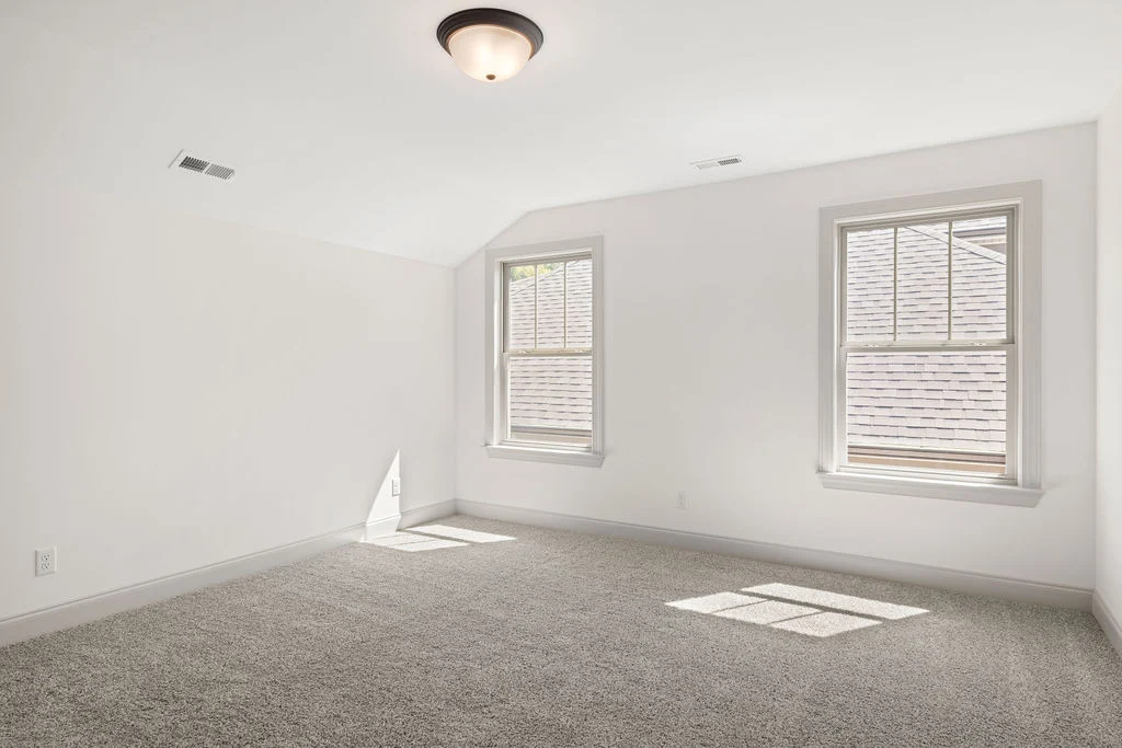 Bright, empty room with two windows, cream walls, and carpeted floor, designed by Pratt Home Builders in Chattanooga TN.