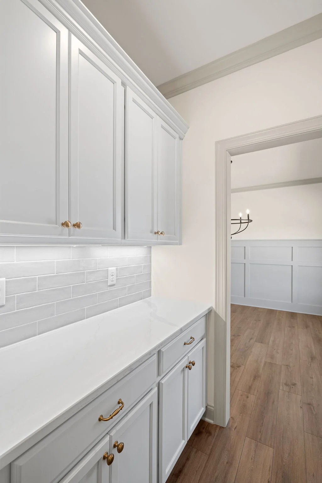 Elegant white cabinetry with gold handles, marble countertop, and tile backsplash by Pratt Home Builders in Chattanooga TN. Wood floor leads to dining