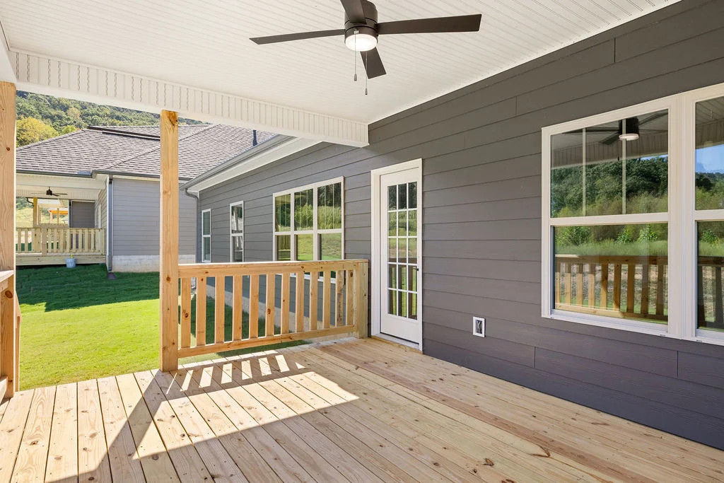 Wooden deck with ceiling fan, part of a gray exterior by Pratt Home Builders in Chattanooga TN, overlooking a grassy yard and mountains.