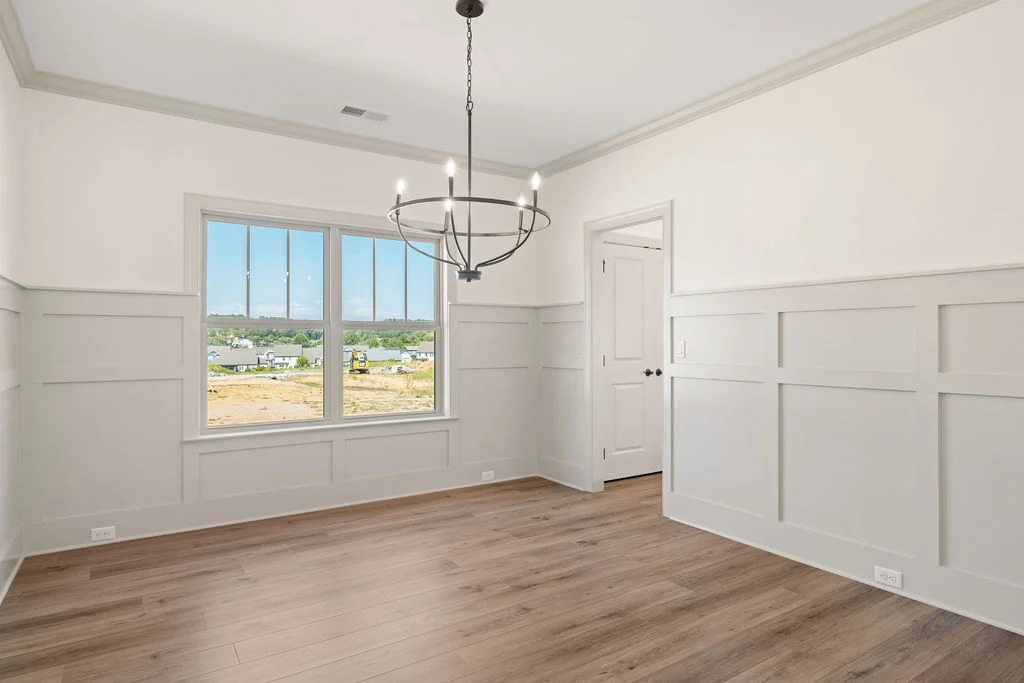 Bright, empty room with wood flooring, elegant molding, and a modern chandelier, showcasing Pratt Home Builders in Chattanooga TN.