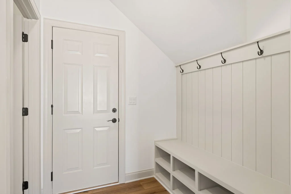 White mudroom with storage bench and coat hooks by Pratt Home Builders in Chattanooga, TN. Bright and minimal design.