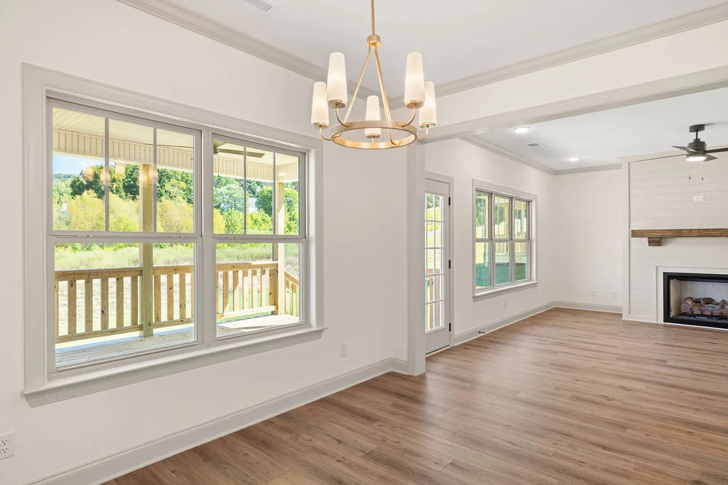 Spacious, sunlit room with large windows, light wood floors, a chandelier, and a fireplace. Built by Pratt Home Builders in Chattanooga TN.