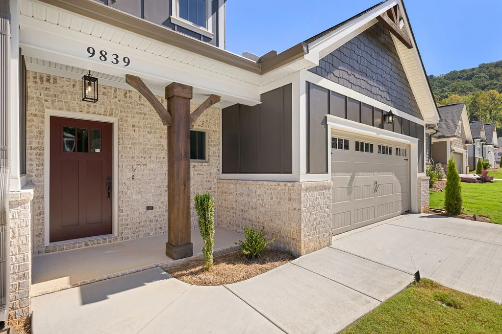 Modern home exterior with brick facade, wooden post, and overhead garage by Pratt Home Builders in Chattanooga TN, set in a residential neighborhood.