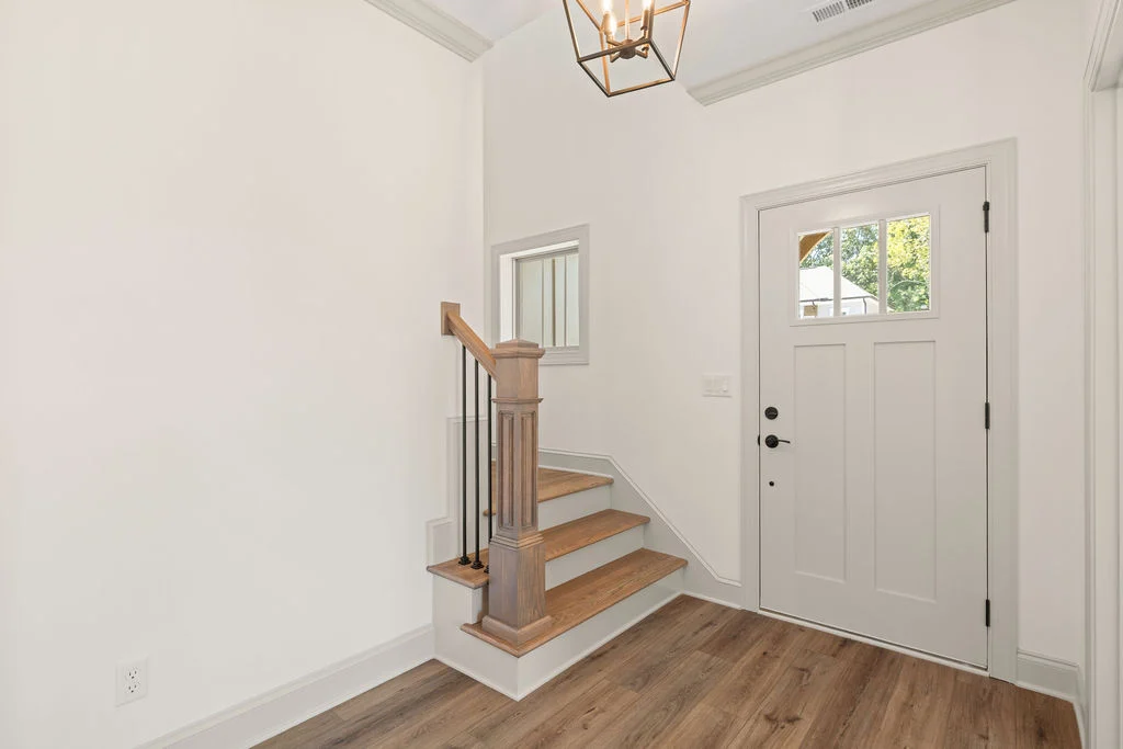 Bright entryway with wooden stairs, white door, and lantern light fixture by Pratt Home Builders in Chattanooga TN.