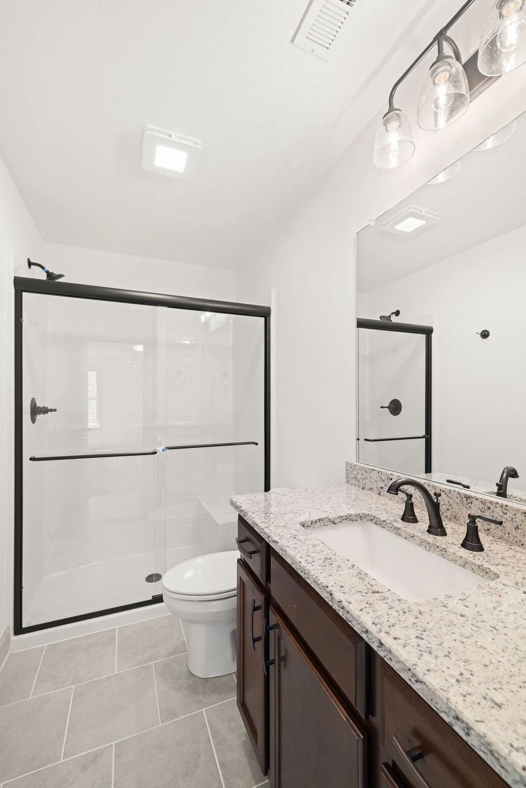 Modern bathroom with granite countertop, dark wood vanity, black fixtures, and glass shower by Pratt Home Builders in Chattanooga TN.