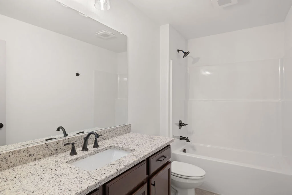 Modern bathroom with granite countertop, dark fixtures, large mirror, and white bathtub. Design by Pratt Home Builders in Chattanooga TN.