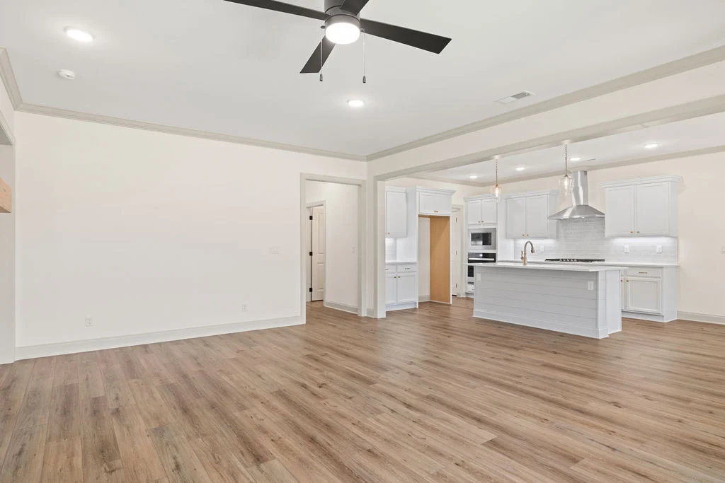 Open-concept kitchen and living area by Pratt Home Builders in Chattanooga, TN, featuring wood floors, white cabinets, and a ceiling fan.