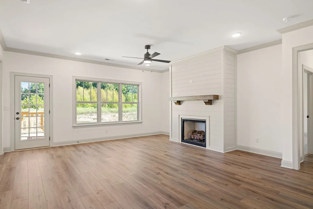 Bright living room with light wood flooring, fireplace, large window, and patio door. Designed by Pratt Home Builders in Chattanooga, TN.