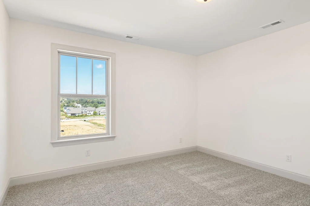Unfurnished room with white walls, carpeted floor, and window view of suburban homes by Pratt Home Builders in Chattanooga TN.