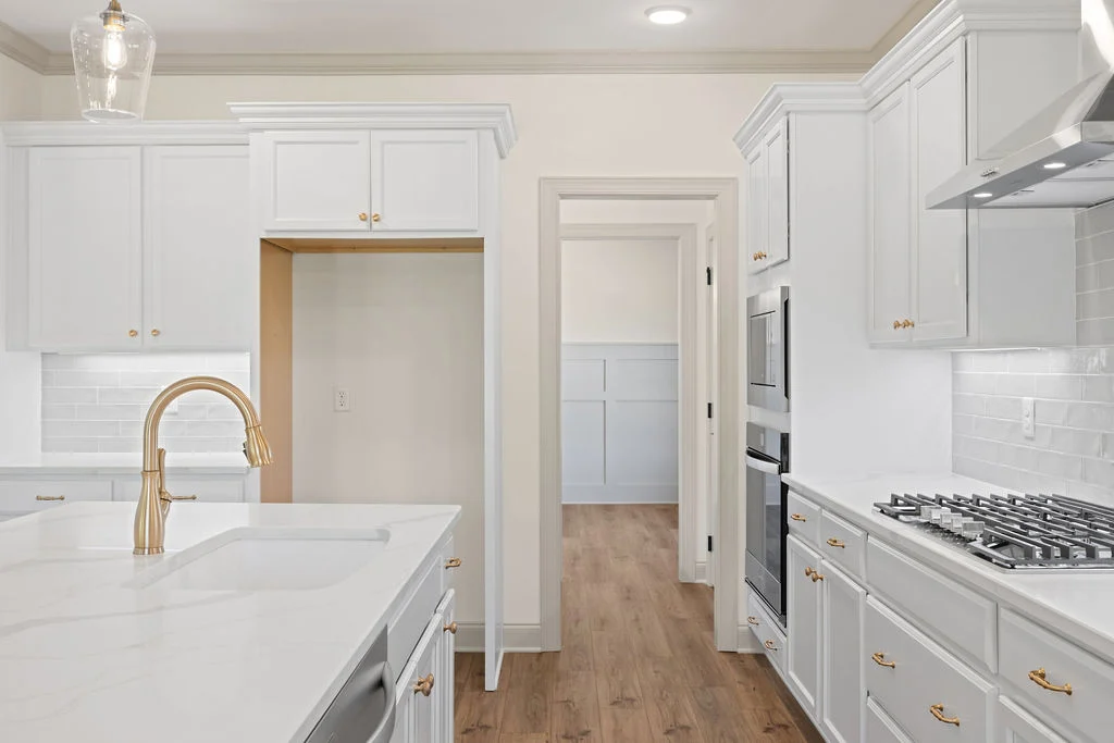 Bright kitchen by Pratt Home Builders in Chattanooga TN, featuring white cabinets, marble countertops, gold fixtures, and wooden flooring.