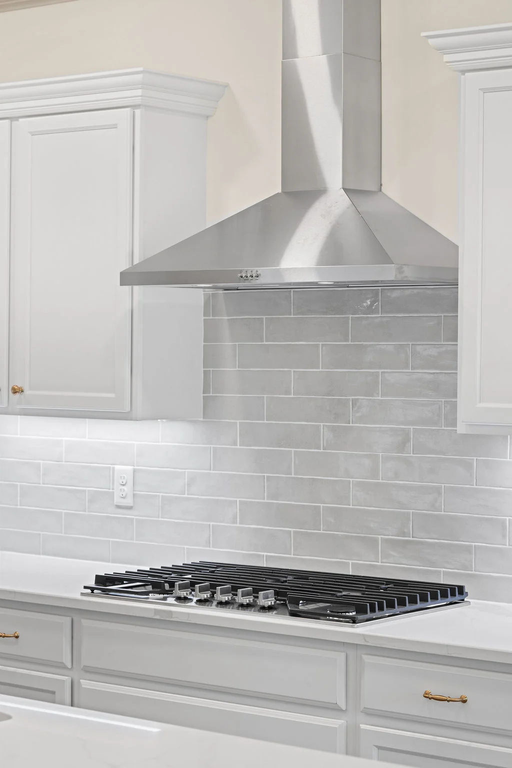 Modern kitchen with stainless steel range hood, white cabinets, and glossy tiled backsplash by Pratt Home Builders in Chattanooga TN.