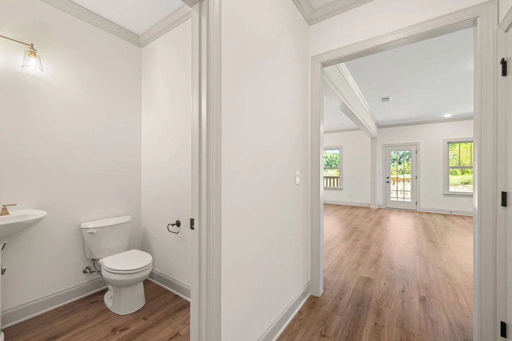 Spacious modern interior by Pratt Home Builders in Chattanooga TN, featuring a bathroom and a bright living room with wood flooring.