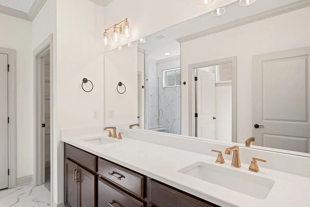 Sleek bathroom with dual sinks, gold fixtures, marble flooring, and spacious shower. Designed by Pratt Home Builders in Chattanooga TN.