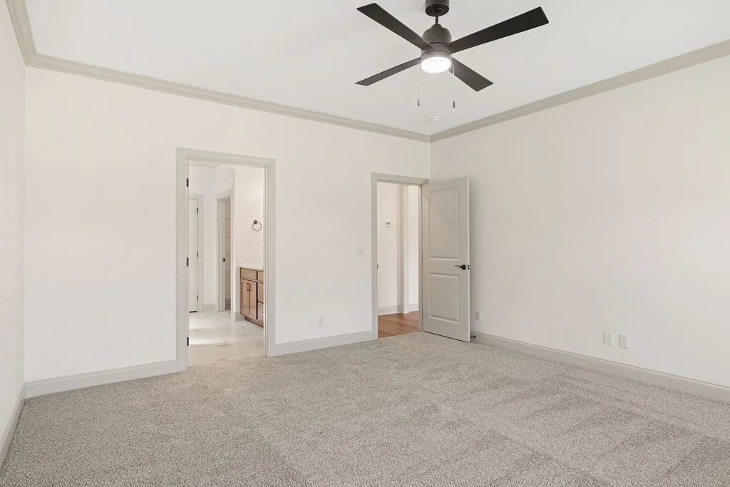 Spacious bedroom with gray carpet, white walls, modern black ceiling fan, and open doors to hallway and bathroom. Pratt Home Builders in Chattanooga T