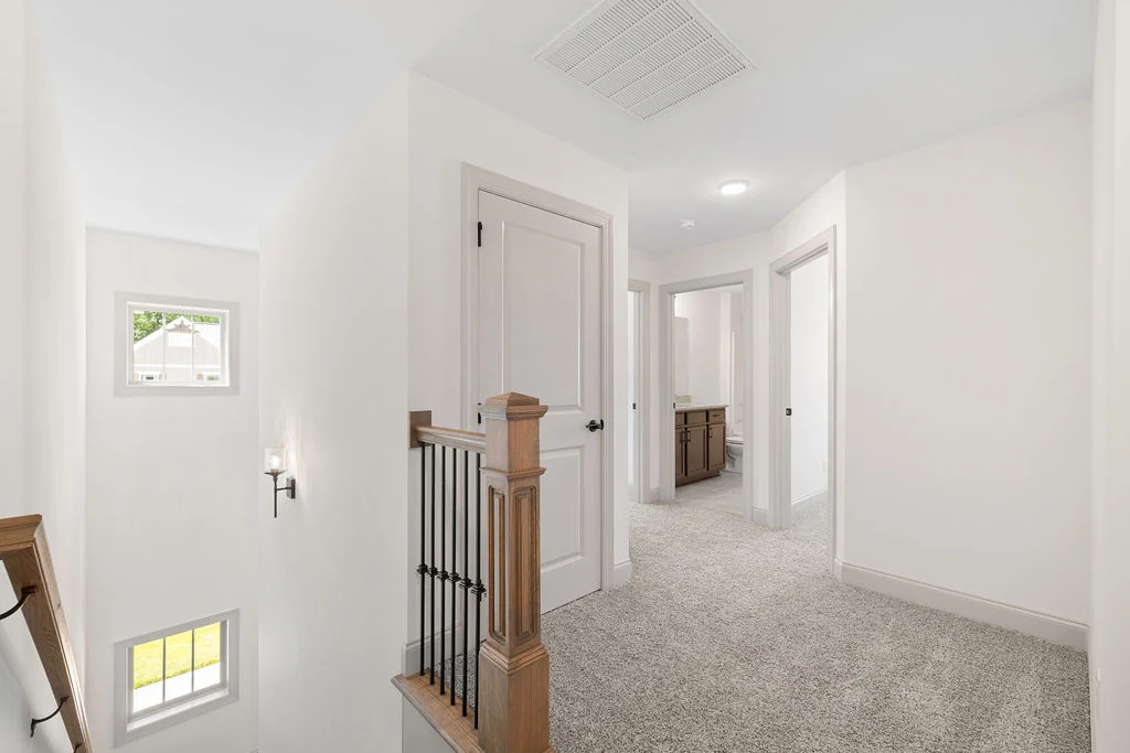 Bright hallway with beige carpet, wooden railing, and multiple doorways in a home by Pratt Home Builders in Chattanooga TN.