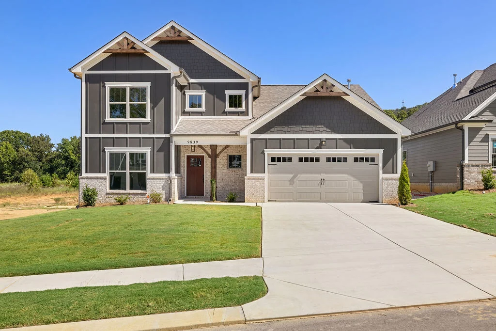 Modern two-story house with gray siding, white trim, and a two-car garage by Pratt Home Builders in Chattanooga, TN, nestled in a suburban setting.