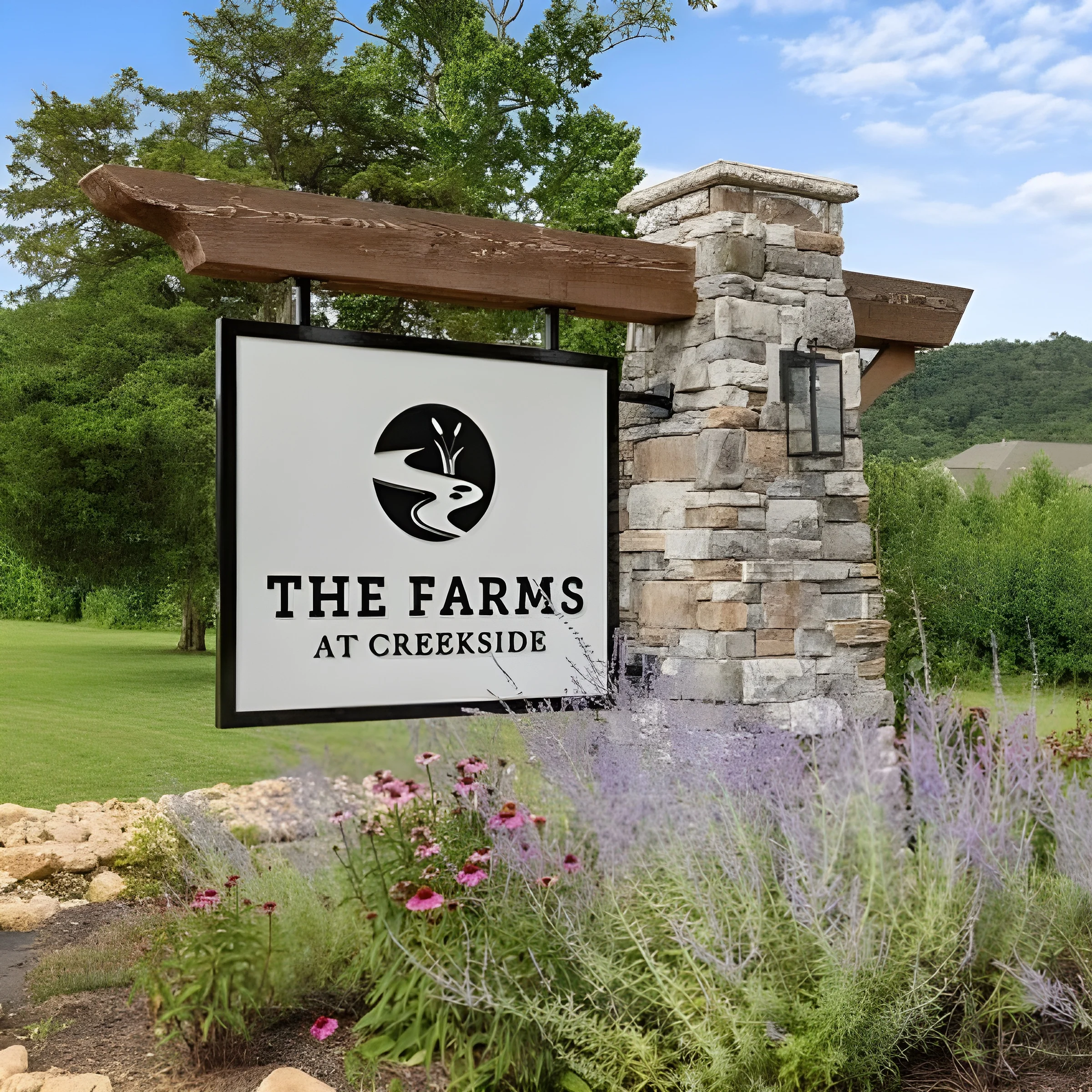 Sign reading "The Farms at Creekside" mounted on a stone pillar, surrounded by lush greenery and flowers; a Pratt Home Builders project in Chattanooga