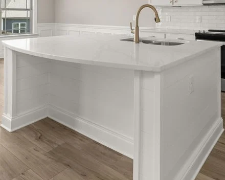 Modern kitchen island with white countertop and gold faucet, designed by Pratt Home Builders in Chattanooga TN. Light wood flooring and backsplash.