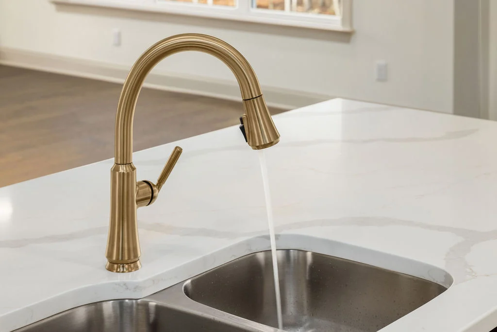Elegant gold kitchen faucet over double sink with water flowing, featuring designs by Pratt Home Builders in Chattanooga TN.