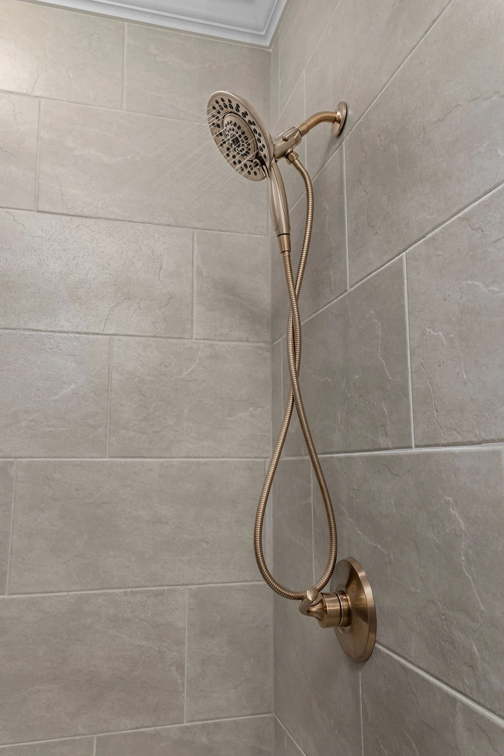 Elegant brass showerhead and hose set against beige tile wall, designed by Pratt Home Builders in Chattanooga TN.