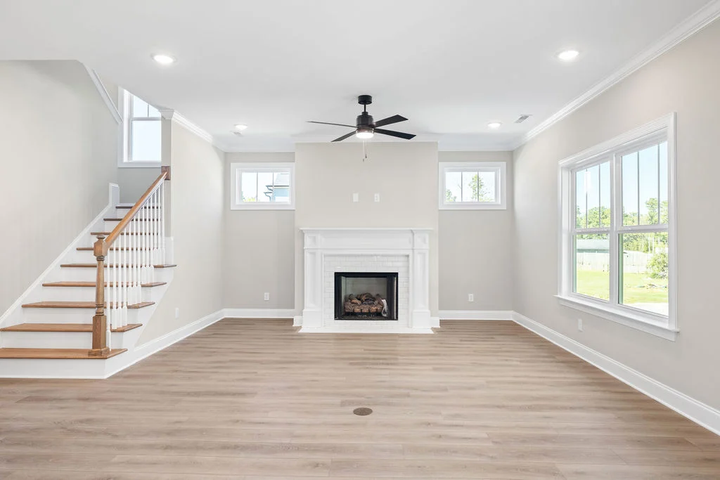 Spacious living room by Pratt Home Builders in Chattanooga, TN; features light wood flooring, a fireplace, ceiling fan, and large windows.