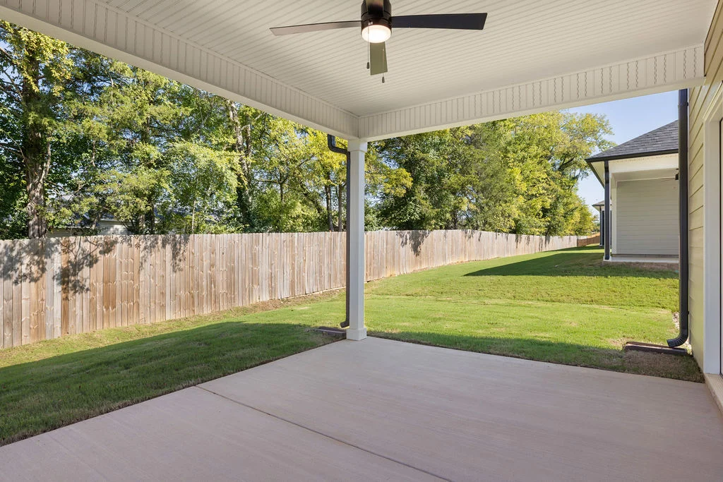 Covered patio with ceiling fan overlooking a grassy backyard and wooden fence, built by Pratt Home Builders in Chattanooga TN.