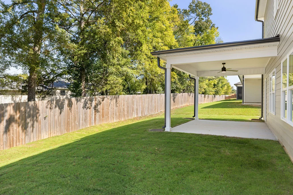 Covered patio with ceiling fan adjacent to a grassy yard, enclosed by a wooden fence, built by Pratt Home Builders in Chattanooga TN.